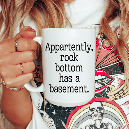 Sarcastic coffee mug featuring Apparently Rock Bottom Has a Basement saying in bold black typewriter-style text.