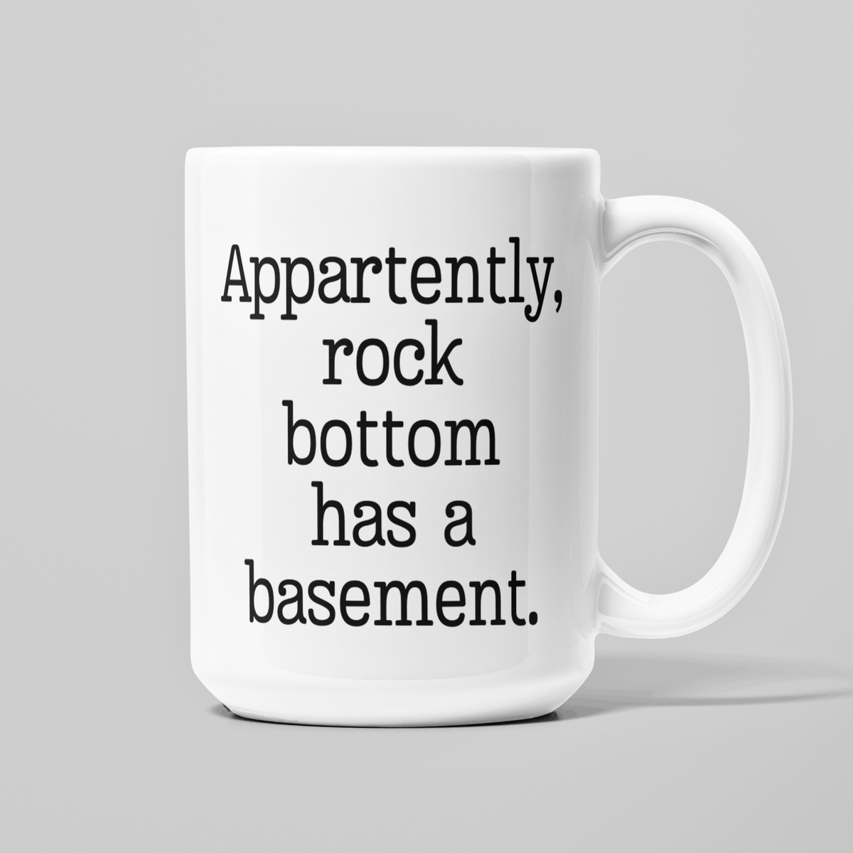 White 15 oz coffee mug with funny Apparently Rock Bottom Has a Basement quote in black lettering.