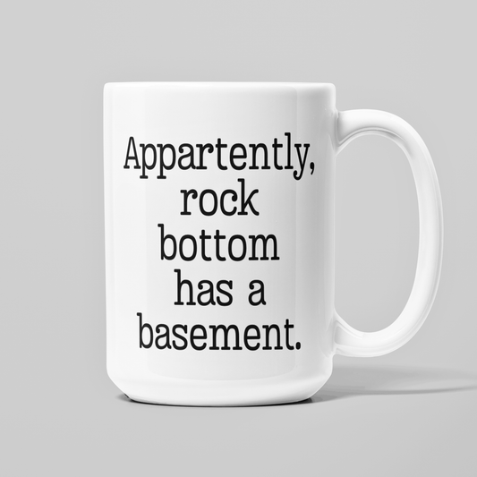 White 15 oz coffee mug with funny Apparently Rock Bottom Has a Basement quote in black lettering.