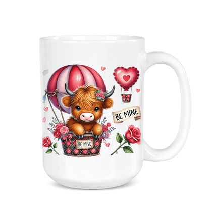 White mug with a cartoon cow in a hot air balloon, surrounded by flowers and 'Be Mine' text on a white background.