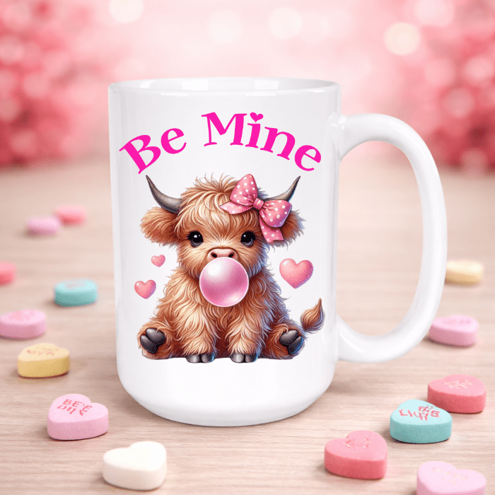 White mug with a cartoon cow blowing a bubble, surrounded by heart-shaped candy on a pink background.