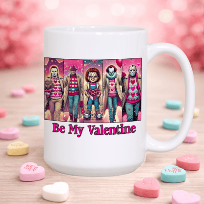 White mug with Valentine-themed design featuring characters in sweaters and 'Be My Valentine' text, surrounded by heart-shaped candy on a wooden surface.