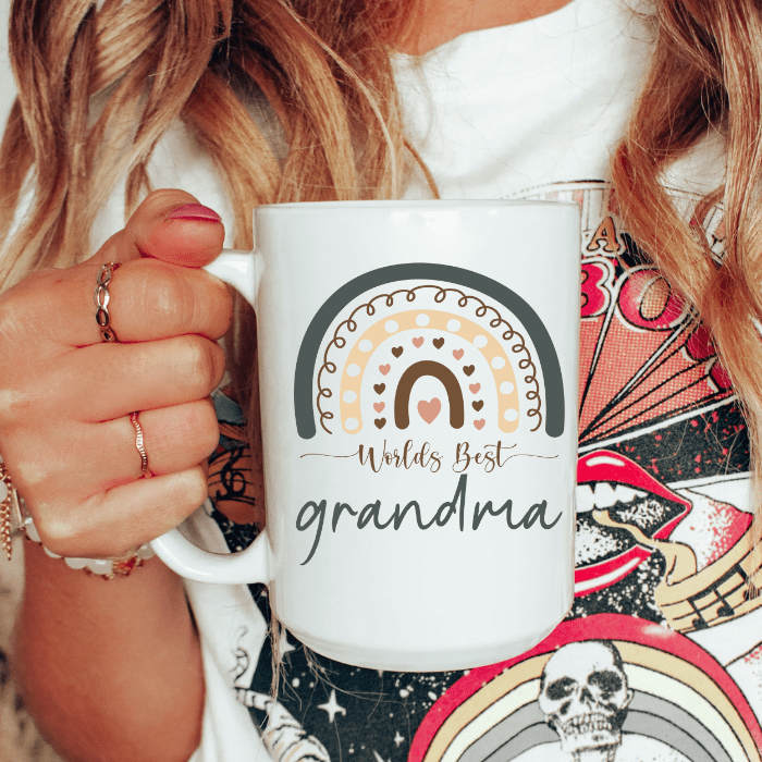 Person holding a mug with 'World's Best Grandma' text and rainbow design.