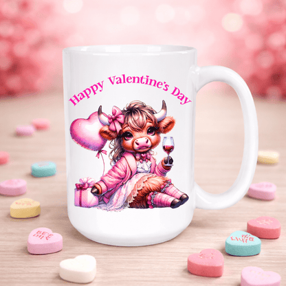 White mug with a cartoon cow holding a heart and glass of wine, surrounded by heart-shaped candies on a pink background.