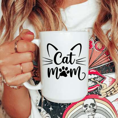 Person holding a white mug with 'Cat Mom' text and paw print design.