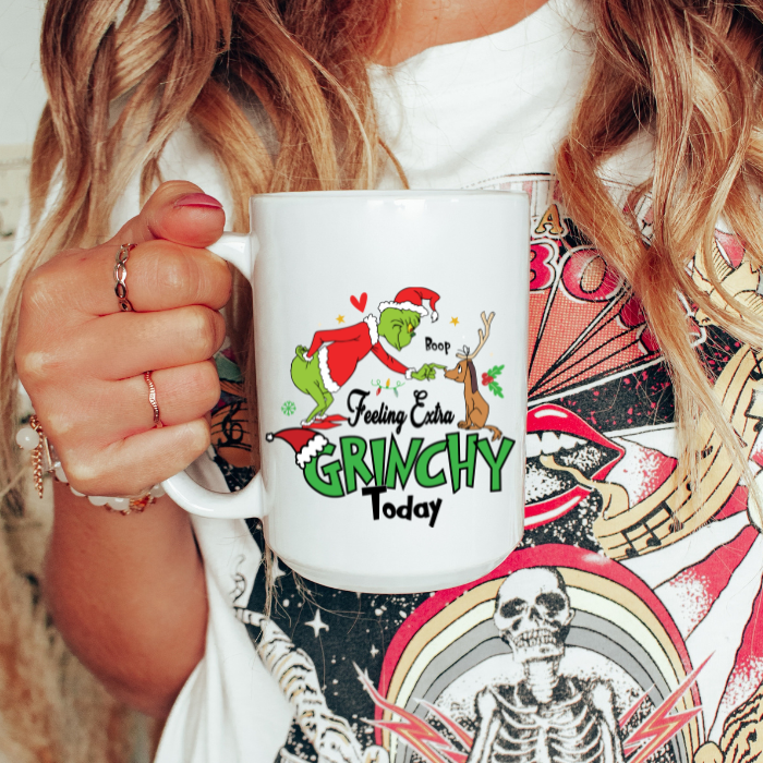 Person holding a mug with a Grinch design and text, wearing a colorful shirt with graphic designs.