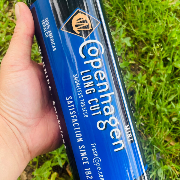 Hand holding a Copenhagen Long Cut tobacco product against a grass background