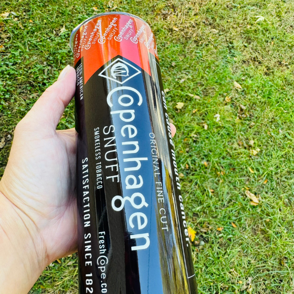 Copenhagen Snuff can held in a hand with grass background