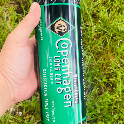 Hand holding a Copenhagen Long Cut Whitewater Green can against a grass background