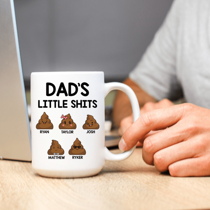 White mug with 'DAD'S LITTLE SHITS' text and poop emoji characters on a desk.
