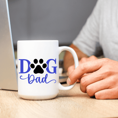 White mug with 'DOG Dad' text and paw print held by a person at a desk.