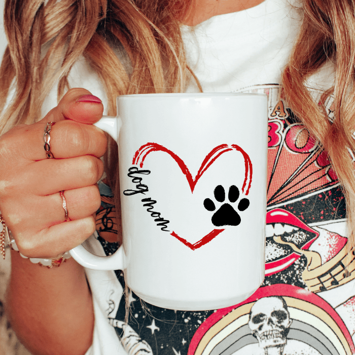 Person holding a white mug with a heart and paw print design, text 'dog mom'.