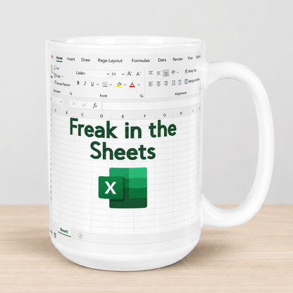 A white ceramic mug printed with an Excel spreadsheet interface and the text 'Freak in the Sheets' in dark green, with the green Excel logo below. The mug is shown on a light wood surface against a neutral gray background.