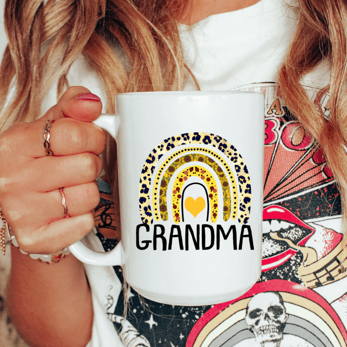 Person holding a white mug with a colorful design and 'GRANDMA' text.