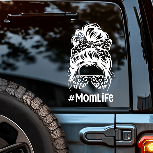 Car window with a '#MomLife' decal featuring a messy bun and sunglasses.