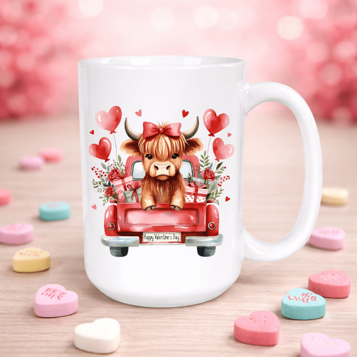 White mug with a cartoon cow in a red truck and Valentine's Day decorations on a wooden surface with heart-shaped candies.