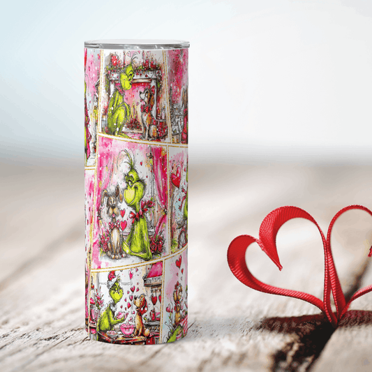 Grinch Tumbler with colorful design featuring characters and hearts, next to a red heart-shaped object on a light background.