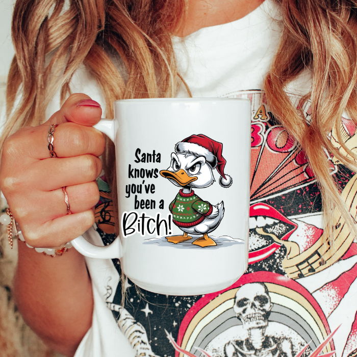 Person holding a mug with a cartoon duck wearing a Santa hat and text, against a colorful background.