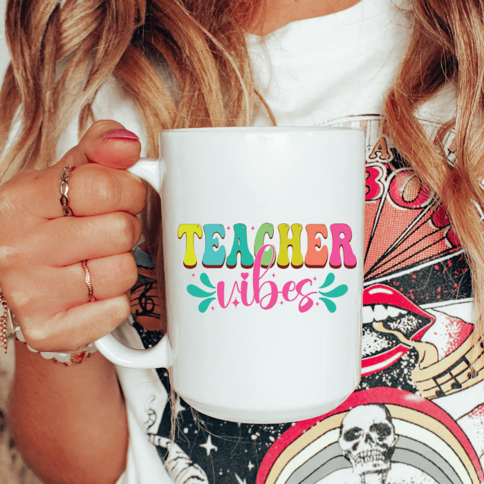 Person holding a white mug with 'TEACHER vibes' text in colorful letters.