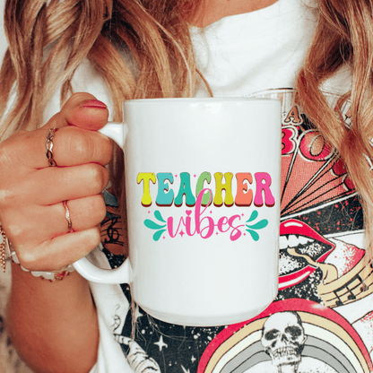 Person holding a white mug with 'TEACHER vibes' text in colorful letters.