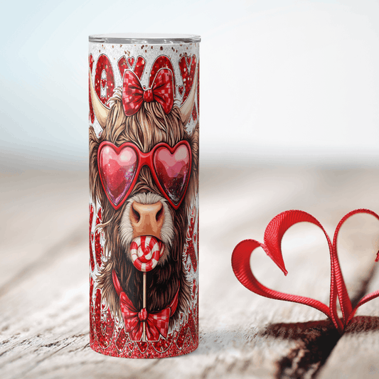 Tumbler with a design of a cow wearing heart-shaped sunglasses and a bow, on a light wooden surface.