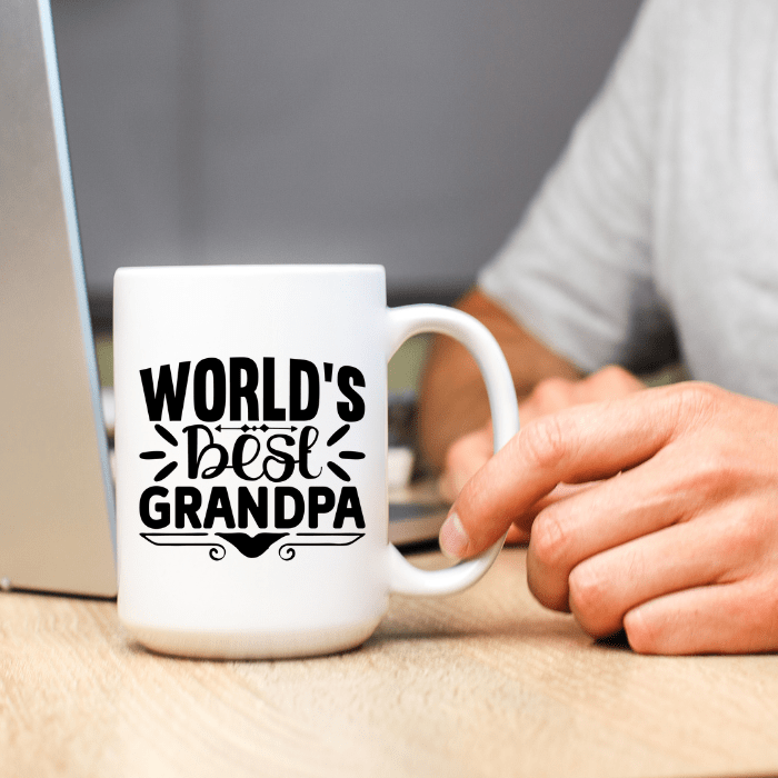 White mug with 'World's Best Grandpa' text held by a person at a desk.